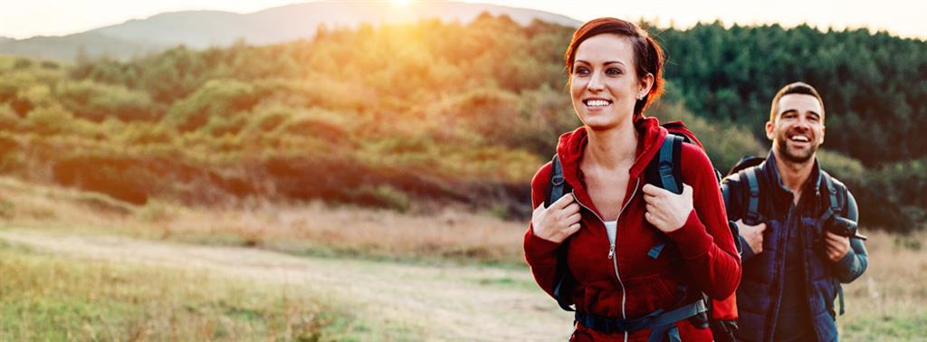 Adult woman and man hiking outdoors carrying their backpacks smiling.